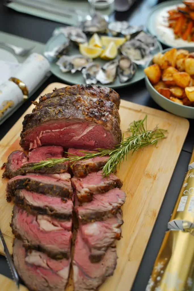 Saftig aufgeschnittenes Rinderfilet als Weihnachtsbraten auf Holzbrett mit Rosmarin und klassischen Beilagen