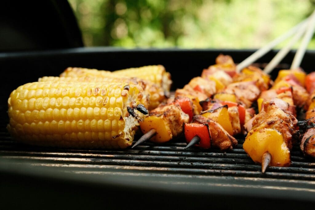 Maiskolben und bunte Gemüsespieße auf dem Grill – vegetarische BBQ-Option
