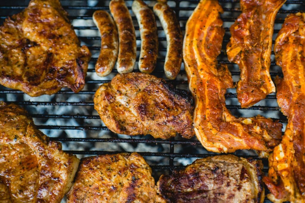 Mariniertes Schweinefleisch und Würste auf dem Grill – bereit zum Wenden