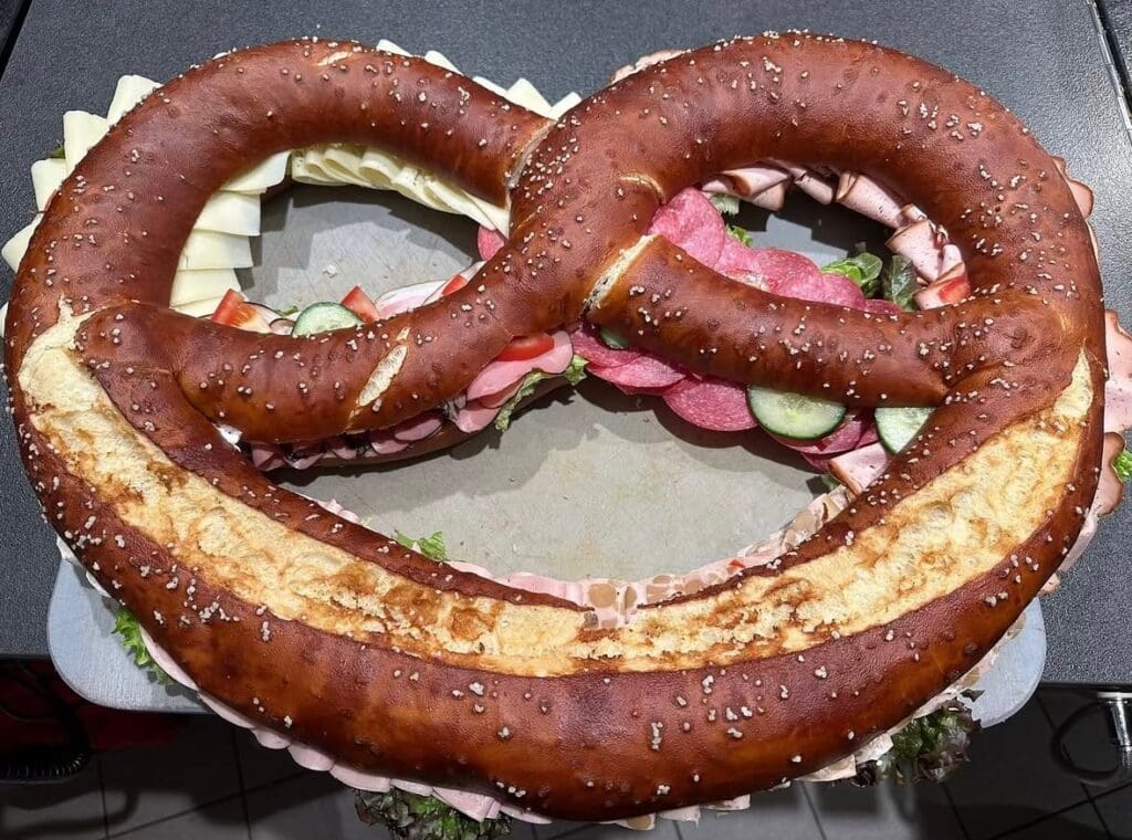 Riesen-Wiesnbreze belegt mit Wurst, Käse und Gemüse – Oktoberfest Catering Spezialität der Metzgerei Stadler in München.